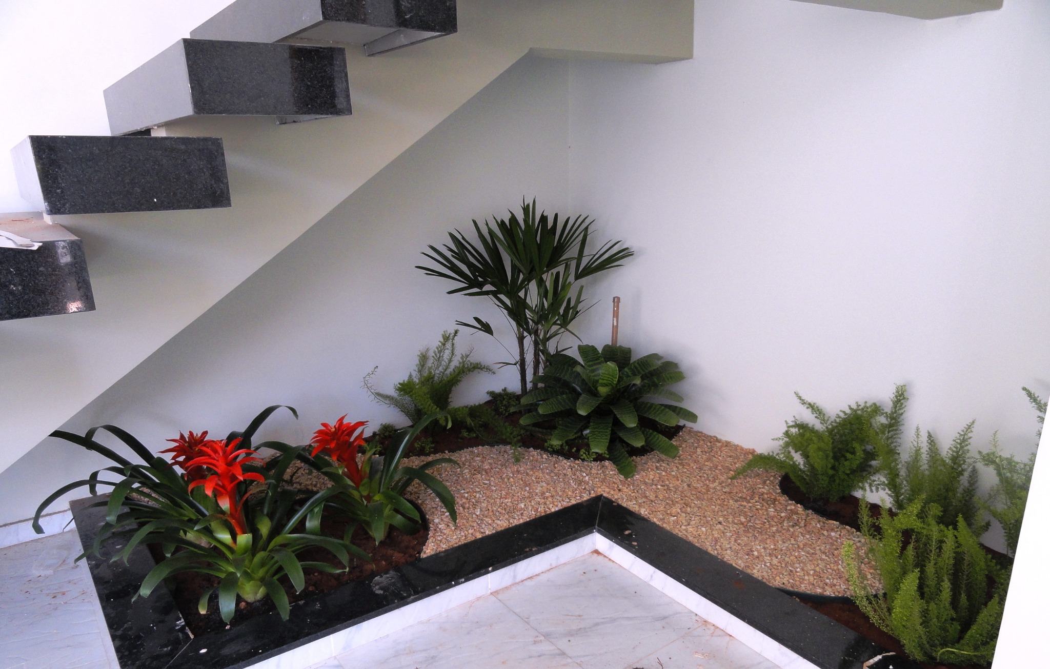 Jardim interno sob escada com bromélias, palmeira e folhagens